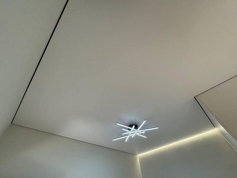 Теневой натяжной потолок с дизайнерской светодиодной люстрой в светлой комнате.