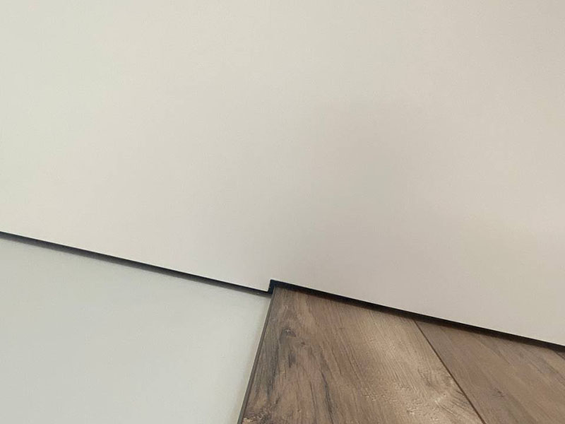 Ровный теневой зазор между натяжным потолком и стеновой панелью с фактурой дерева.