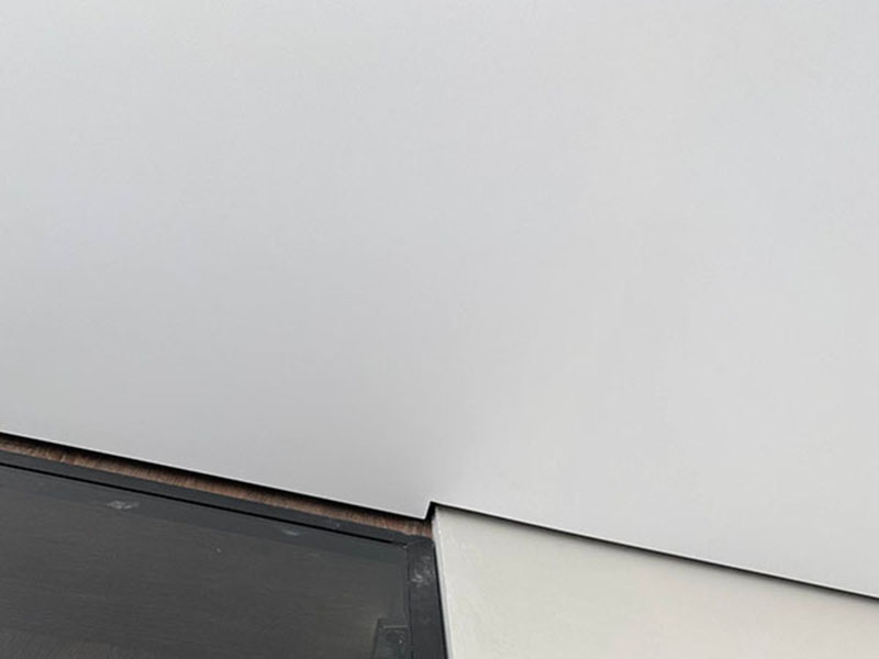 Узел примыкания теневого натяжного потолка к белой стене и темной мебельной конструкции.