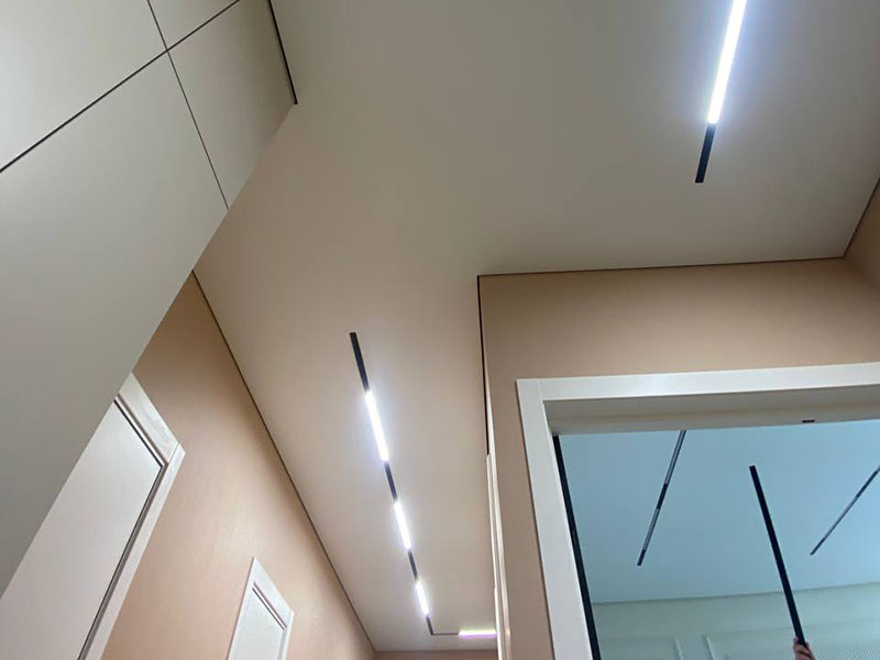 Встроенная черная трековая система с LED-лентами в натяжном потолке в коридоре