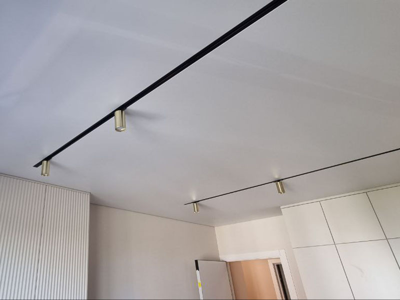 Черный шинопровод с золотистыми цилиндрическими спотами на натяжном потолке в интерьере, Гродно